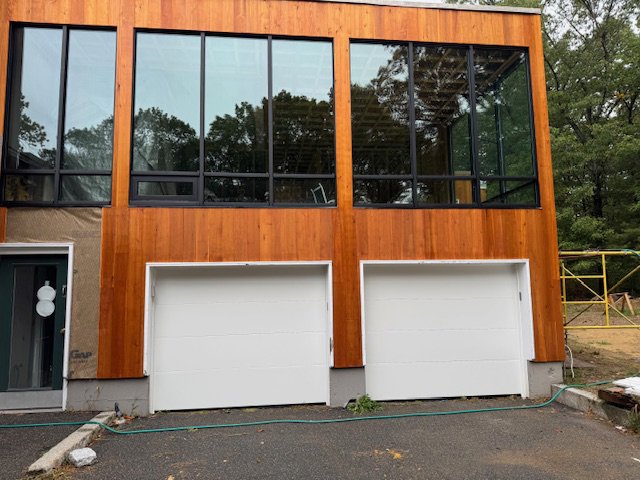 Two white garage doors installed on a modern wooden-sided home by J.A. Overhead Door in Westfield, MA.