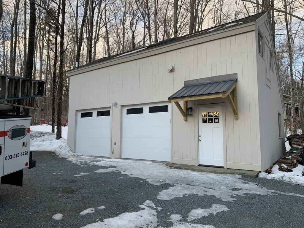Two white garage doors with top windows installed on a building in a winter setting by J.A. Overhead Door in Westfield, MA.