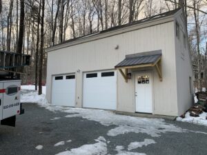 Two white garage doors with top windows installed on a building in a winter setting by J.A. Overhead Door in Westfield, MA.