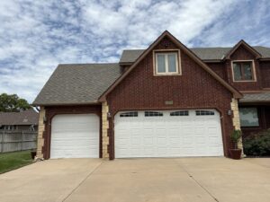 Two newly installed white panel garage doors on a brick residential home by The Door Pros in Wichita, KS