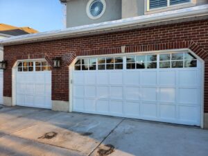 Two white paneled garage doors on a brick residential home, installed by Layton Doors in West Jordan, UT.