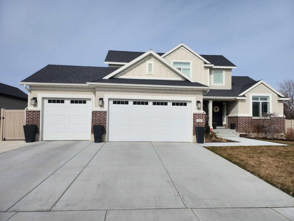A residential home featuring two newly installed white paneled garage doors by Layton Doors in West Jordan, UT.