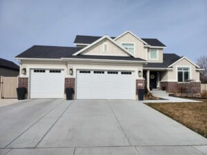 A residential home featuring two newly installed white paneled garage doors by Layton Doors in West Jordan, UT.