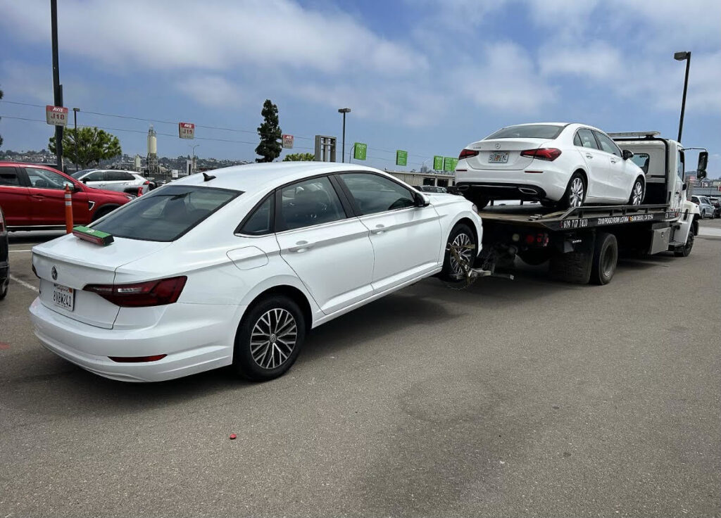 Two white sedans being towed, one on a flatbed and one by wheel lift, by Cali kings Towing in San Diego, CA.