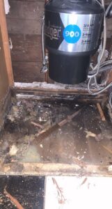 Severe water damage and debris under a sink with a garbage disposal, requiring remediation by Quality Remediation llc in Everett, WA.