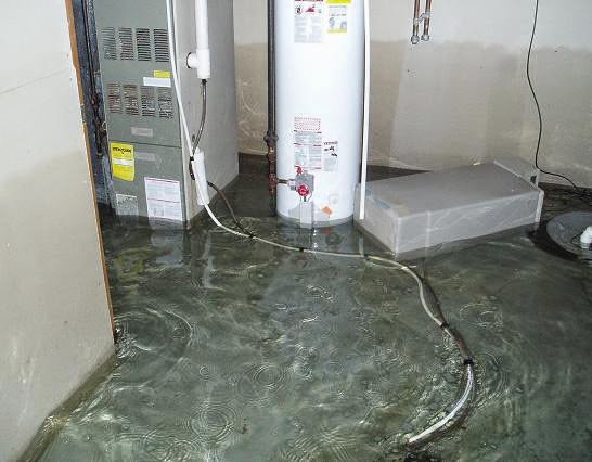 A utility room with a water heater and furnace surrounded by standing water, showing significant water damage in Oakland, CA by One Call Services of Oakland.
