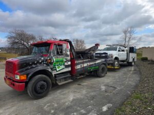 A white utility truck being towed by a wrecker from Gem State Towing and Recovery in Caldwell, ID.