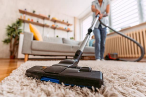 A vacuum cleaner on a plush carpet, with a person vacuuming in the background for Peak&co Cleaners in Great Falls, MT.