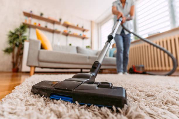 A vacuum cleaner on a plush carpet, with a person vacuuming in the background for Peak&co Cleaners in Great Falls, MT.