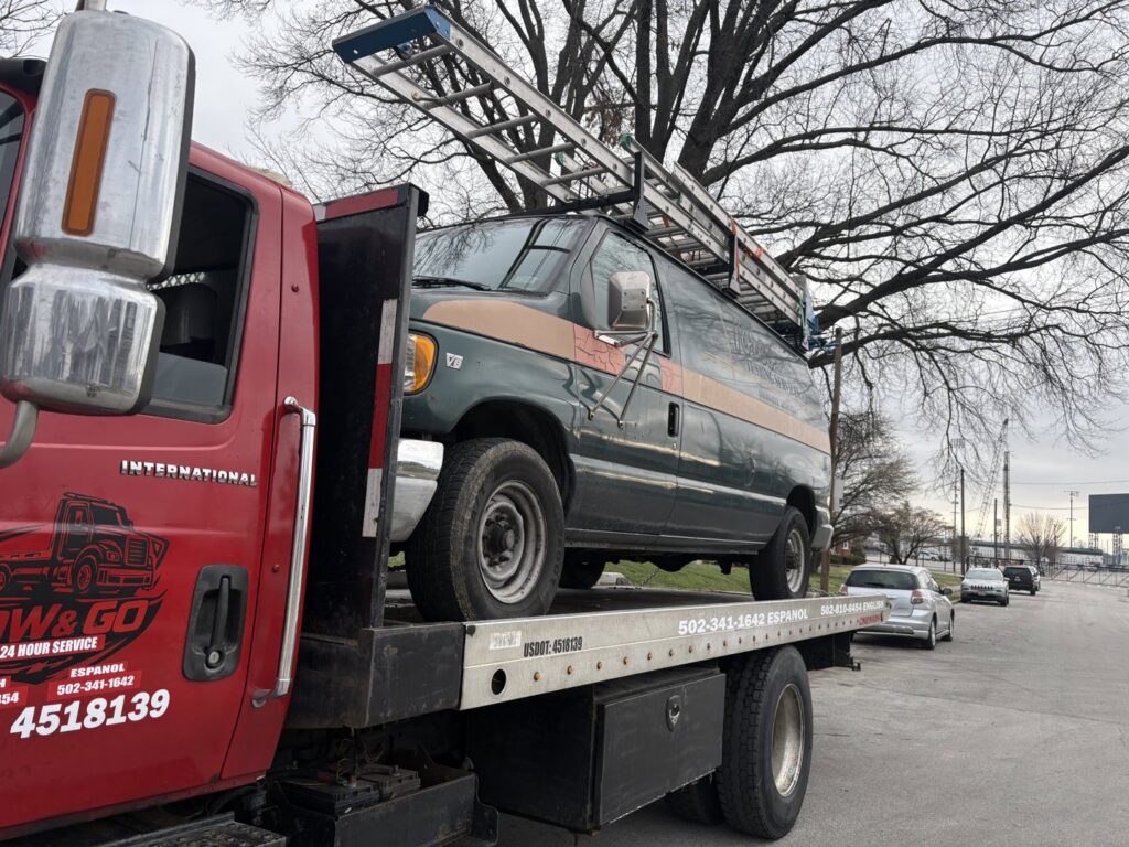 A work van with a ladder on its roof being towed on a flatbed truck by Tow & go in Louisville, KY.