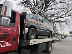 A work van with a ladder on its roof being towed on a flatbed truck by Tow & go in Louisville, KY.