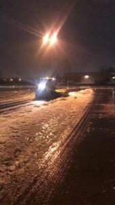 A snow removal vehicle actively plowing slushy snow and ice from a parking lot at night for Appleton Snow Removal in Appleton, WI.