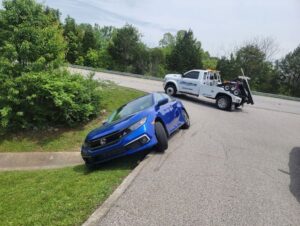 A TowTime Towing and Recovery wrecker truck preparing to recover a blue Honda Civic stuck off the road in Bloomington, IN.