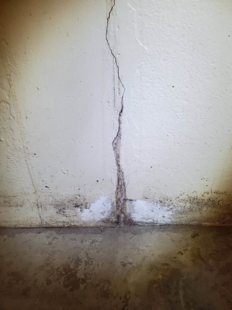 A vertical crack on an interior wall illuminated by a flashlight, indicating a potential foundation issue for Northeast Wisconsin Waterproofing, LLC in Green Bay, WI.
