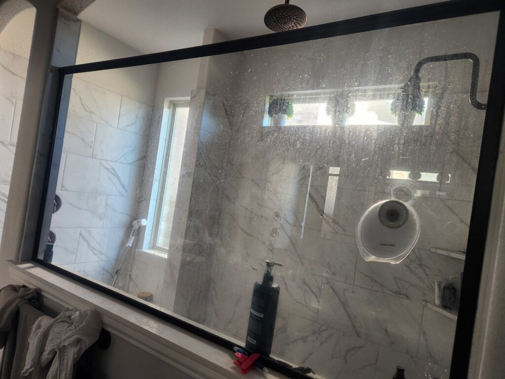 A very dirty shower glass panel covered in soap scum and water stains, ready for cleaning by Rita's cleaning in Fort Worth, TX.