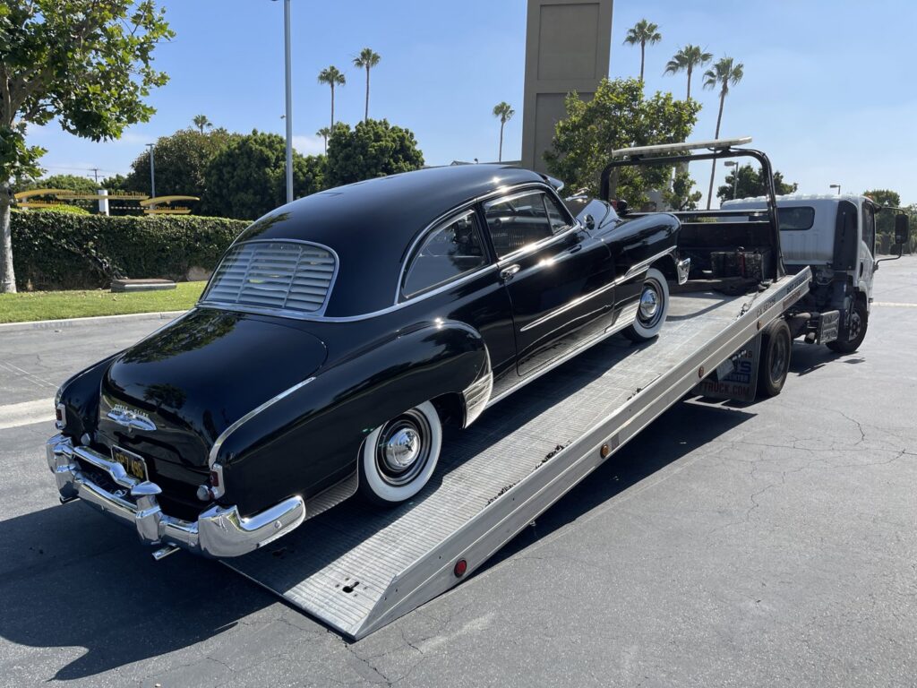 A black vintage car being loaded onto a flatbed tow truck by Leos Towing Service in Anaheim, CA.