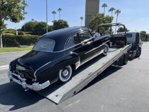 A black vintage car being loaded onto a flatbed tow truck by Leos Towing Service in Anaheim, CA.