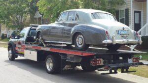 A flatbed tow truck from Raleigh Towing & Recovery transporting a vintage car in Raleigh, NC.