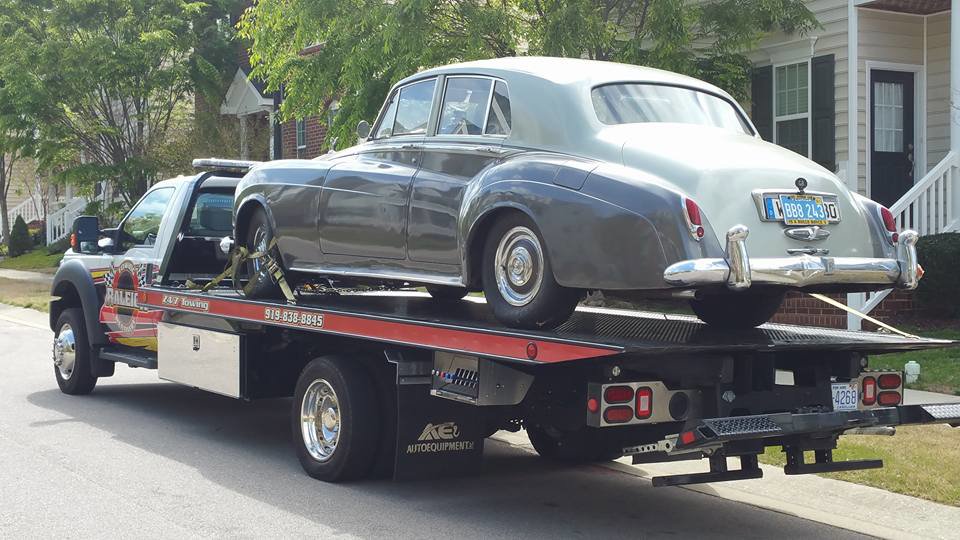 A flatbed tow truck from Raleigh Towing & Recovery transporting a vintage car in Raleigh, NC.