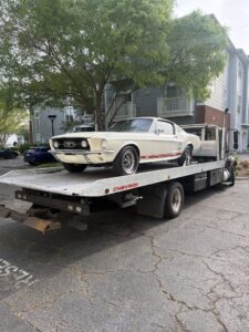 A vintage white Ford Mustang loaded onto a flatbed tow truck from Bullcity Towing & Services LLC in Durham, NC.