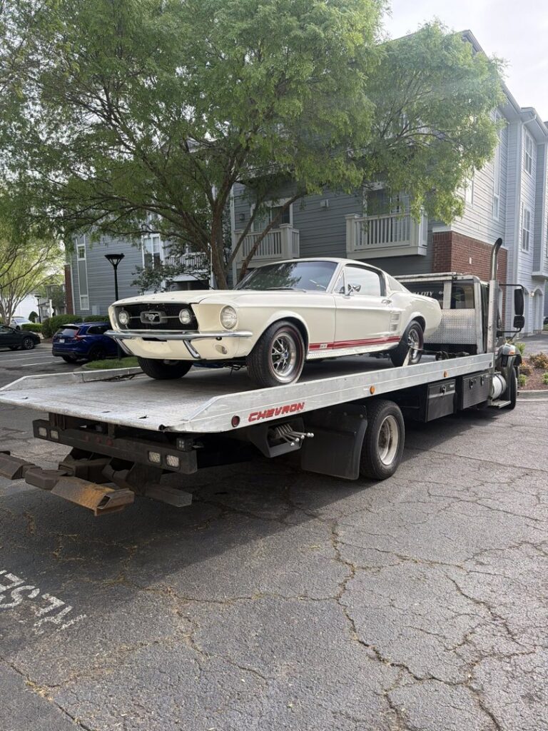 A vintage white Ford Mustang loaded onto a flatbed tow truck from Bullcity Towing & Services LLC in Durham, NC.