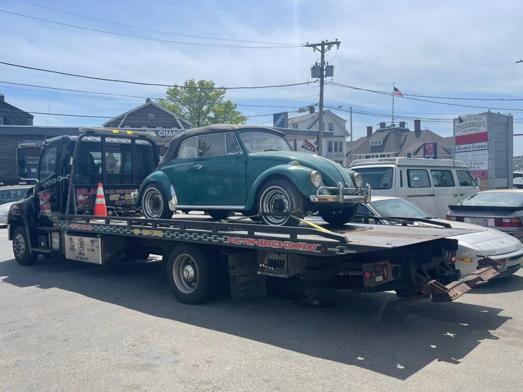 A vintage green Volkswagen Beetle being transported on a flatbed tow truck by Milan Towing inc. in Milan, MI.
