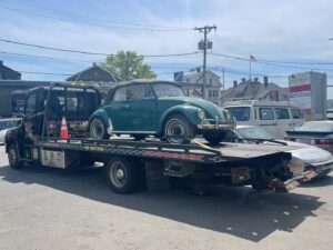 A vintage green Volkswagen Beetle being transported on a flatbed tow truck by Milan Towing inc. in Milan, MI.