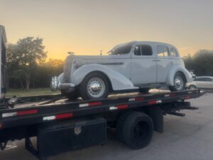 A vintage grey car being transported on a flatbed tow truck by Towing Near Me 247 LLC in Irving, TX.
