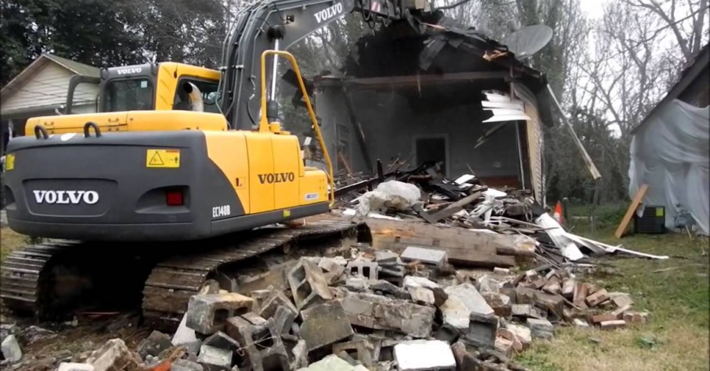 A yellow Volvo excavator actively demolishing a residential house for San Antonio Demolition Pros in San Antonio, TX.