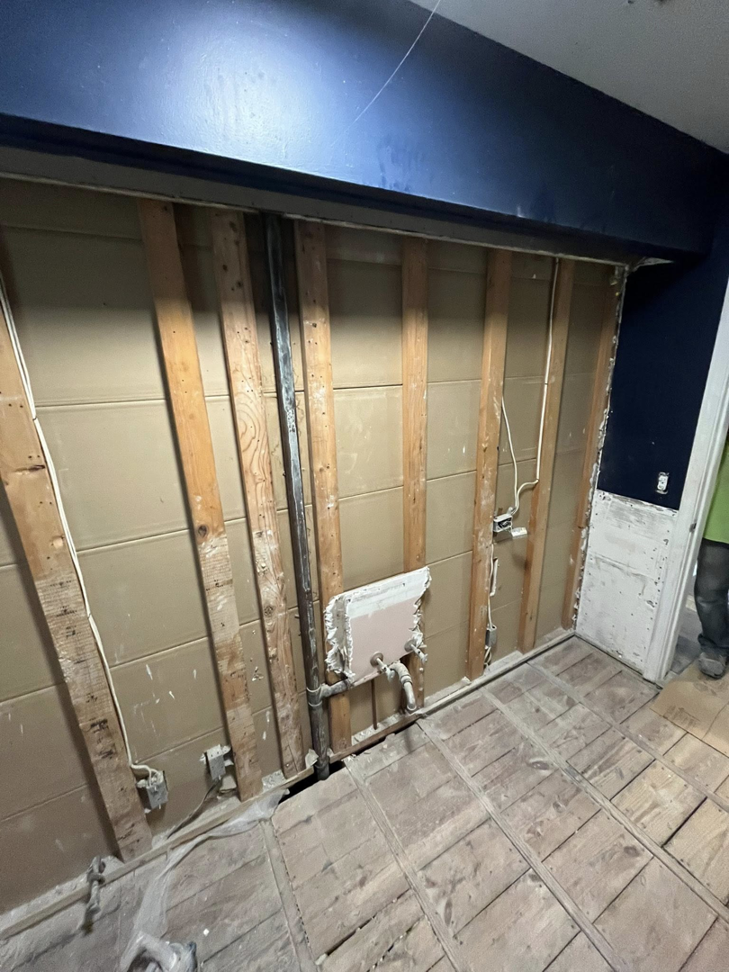 A wall and floor area undergoing demolition due to water damage, exposing studs and subfloor by 24K Restoration in Flint, MI.