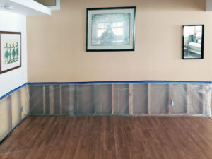 A room with lower walls removed, exposing studs, and plastic sheeting on the floor for water damage remediation by Island Restoration LLC in Kapolei, HI.