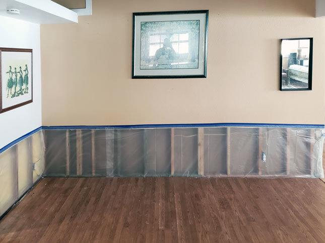 A room with lower walls removed, exposing studs, and plastic sheeting on the floor for water damage remediation by Island Restoration LLC in Kapolei, HI.