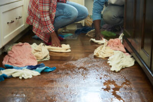 Two individuals cleaning up puddles of water from a flooded wooden floor, a common task for ServiceMaster DSI - Champaign, IL