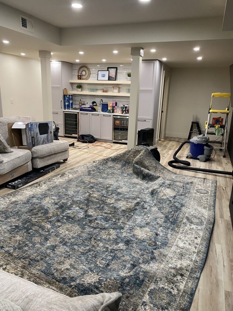 A living room with a rolled-up rug and a wet vacuum, indicating water cleanup in progress by Cowboy Certified Plumbing & Water Cleanup in Lee's Summit, MO.