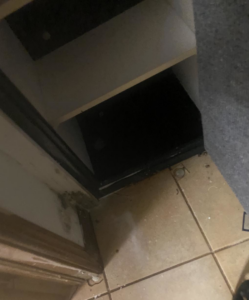 Water damage and mold on the tiled floor and baseboard near a dark opening, showing a need for restoration by 24HR Flood Pros of OKC in Oklahoma City, OK.
