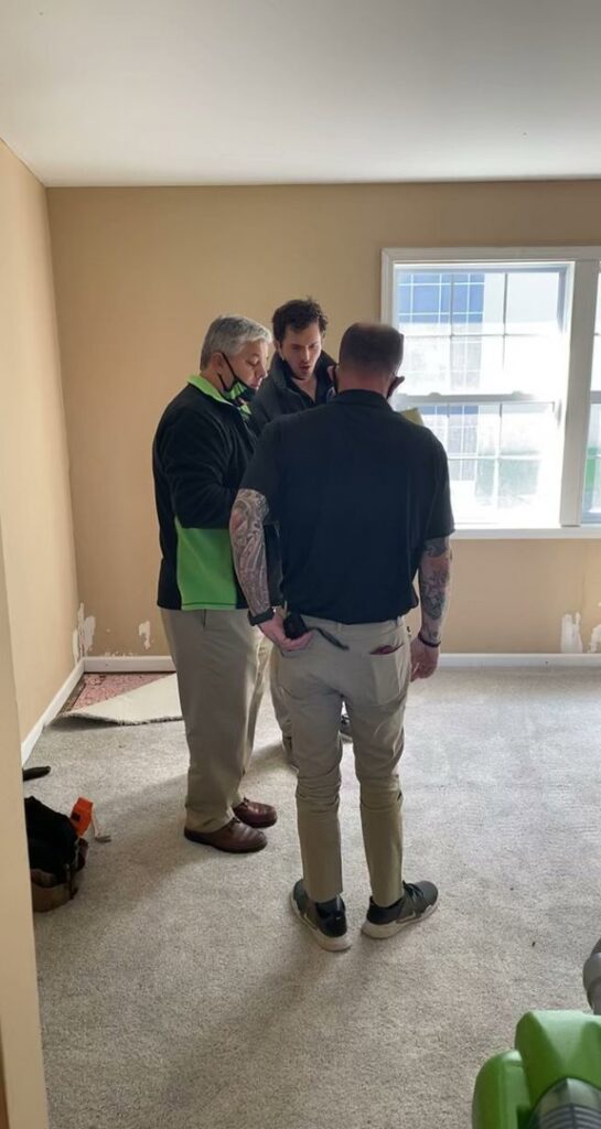 Servpro technicians assessing water damage in a residential room with exposed subfloor and drying equipment in Athens, AL.
