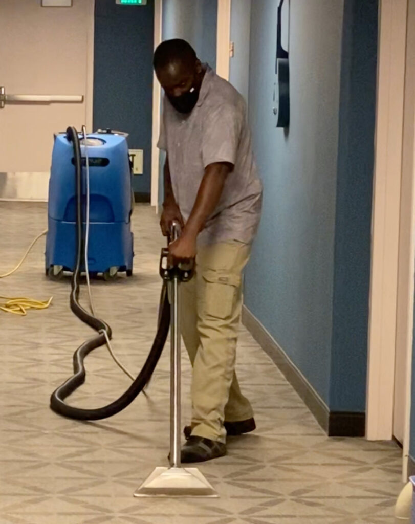 A worker performing water damage carpet extraction with a professional machine for Renue Systems Of Oahu in Honolulu, HI