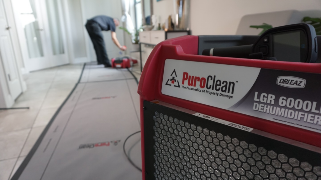 A PuroClean technician setting up a large dehumidifier for water damage restoration in a home in Northport, AL.