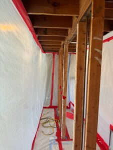 A hallway with plastic containment and exposed studs during water damage demolition by RestoPros of Hartford in West Hartford, CT.