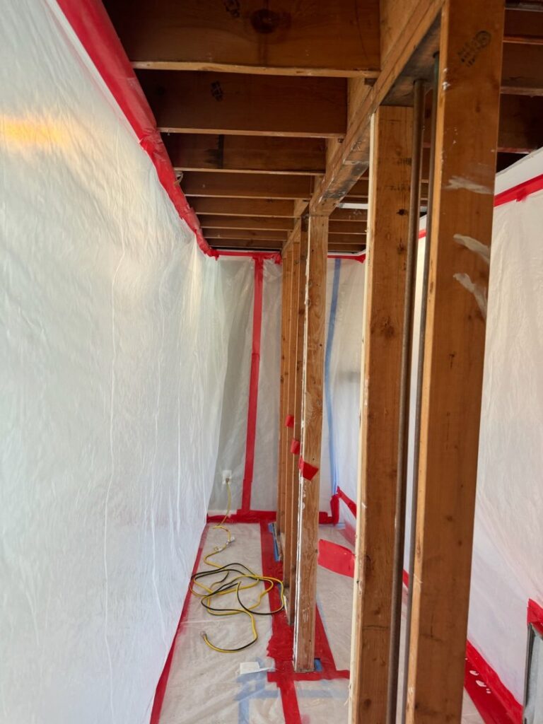 A hallway with plastic containment and exposed studs during water damage demolition by RestoPros of Hartford in West Hartford, CT.