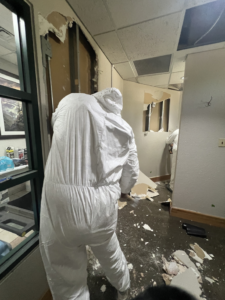 A water damage specialist in a hazmat suit performing demolition and removing damaged drywall for HTS Restoration in El Paso, TX.