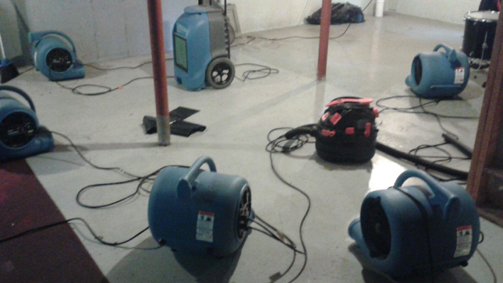 Industrial fans and a dehumidifier drying a basement after water damage by Adams Emergency One in East Providence, RI