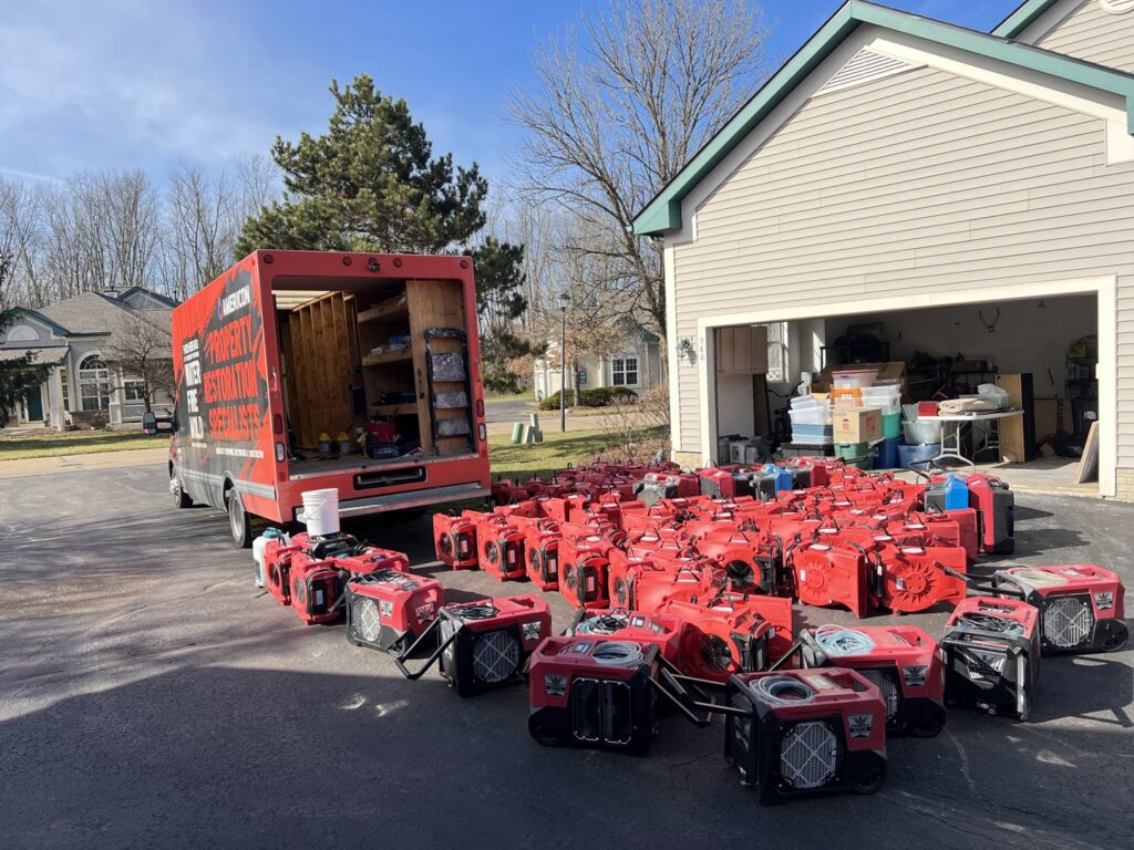 Numerous red air movers and drying equipment lined up on a driveway for water damage restoration by Americon Restoration in Youngstown, OH.