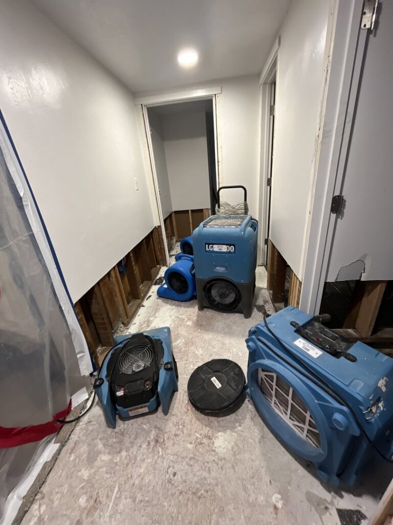 Industrial air movers and dehumidifiers set up in a hallway with exposed wall studs, actively drying out water damage as part of restoration by Standard Restoration in Salt Lake City, UT.