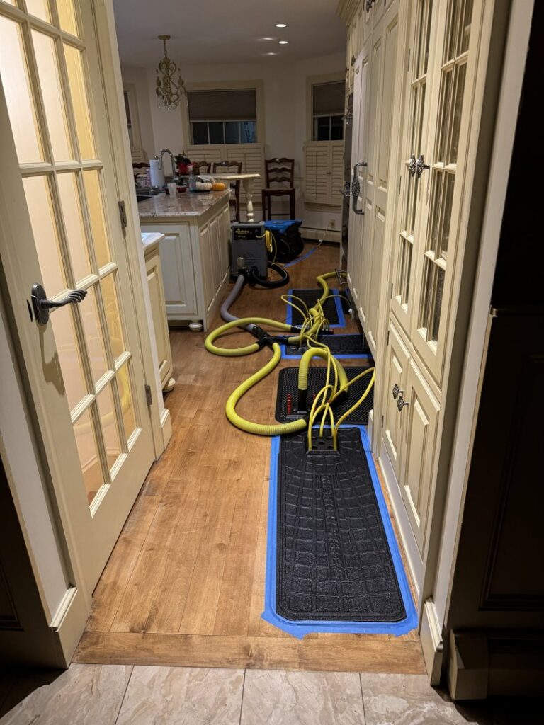 Water damage drying equipment, including hoses and mats, set up in a kitchen and hallway by Clean Care of New England in Cranston, RI