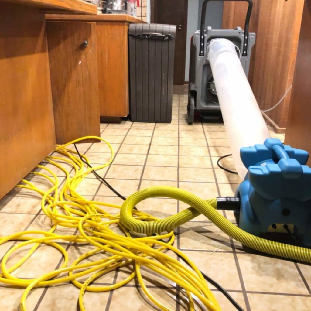 Water damage drying equipment, including an air mover and dehumidifier, set up in a kitchen by Rescue One Restoration in Honolulu, HI.