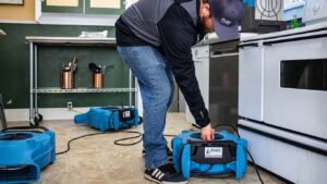 A Pure Restore technician setting up water damage drying equipment in a kitchen in Northglenn, CO.