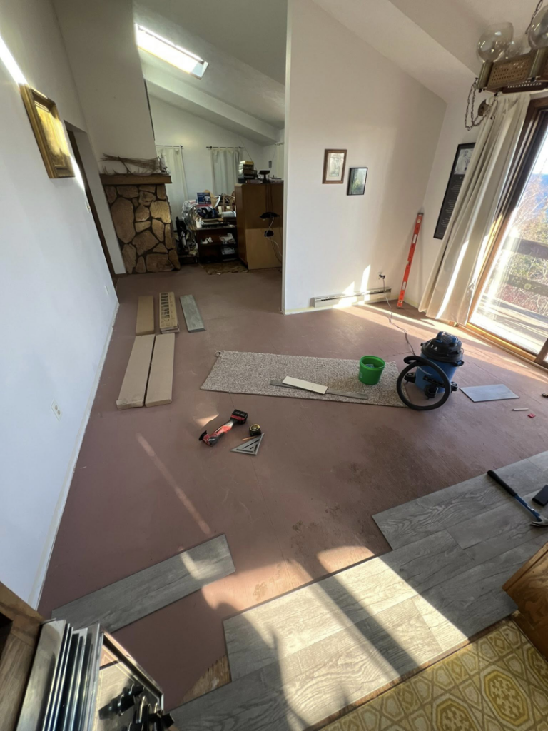 Water damage specialist installing new flooring over underlayment with a shop vac nearby at a job site for Agate Bay Restoration in Two Harbors, MN.