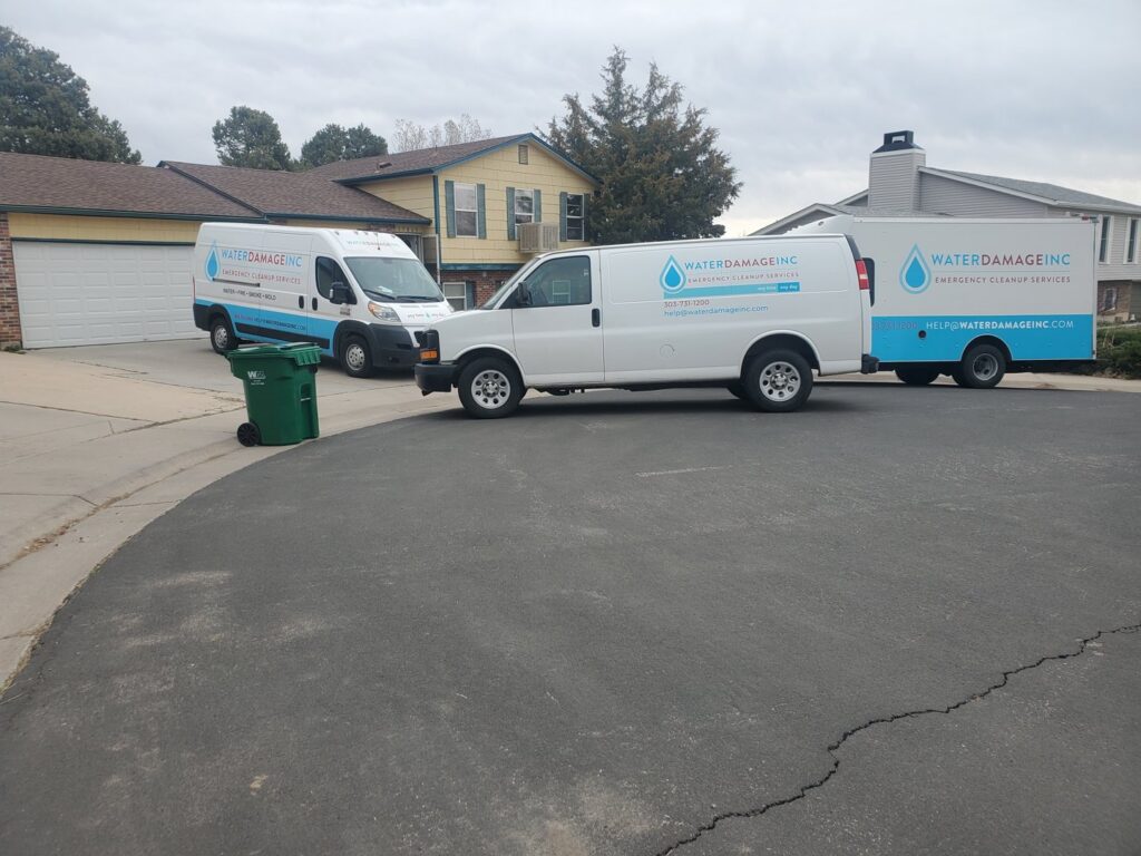 Water Damage, Inc. service vans and trailer parked in a residential area in Denver, CO.