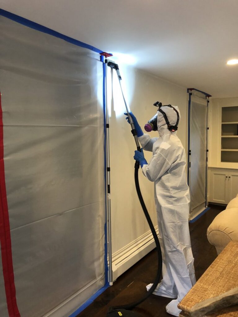 A Green Home Solutions technician in a hazmat suit performing water damage remediation on a wall with containment in Mount Airy, MD.